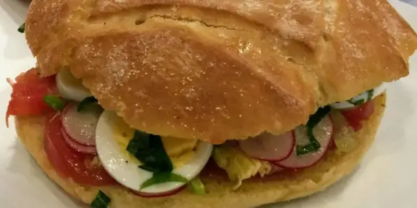 Un délicieux pan bagnat garni de tomates, œufs durs, radis et herbes fraîches. Parfait pour une recette facile et savoureuse.