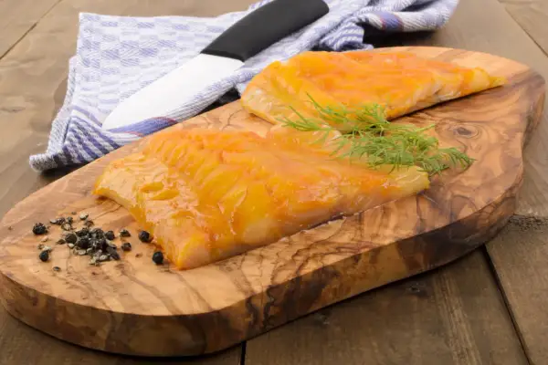 Deux beaux filets de haddock poisson fumé, prêts à être dégustés, sur une planche en bois d'olivier avec de l'aneth et du poivre.
