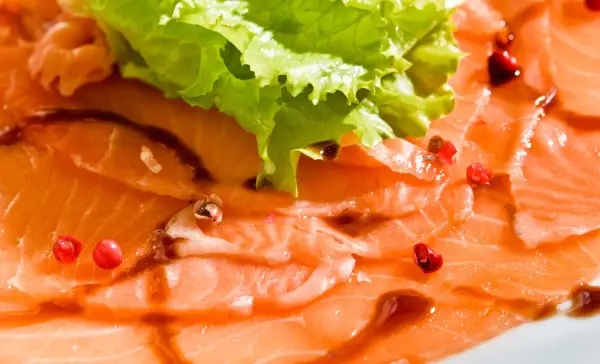 Délicieux carpaccio de saumon, fines tranches de poisson cru, garnies de quelques baies roses et d'une feuille de laitue croquante.