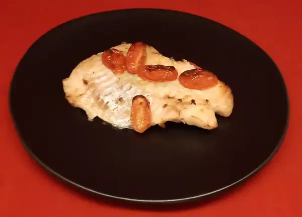 Un filet de dorade sebaste cuit, garni de tomates cerises rôties, servi sur une assiette noire.